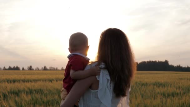 Madre con el bebé en sus brazos de pie contra la puesta de sol en los cálidos rayos del sol — Vídeos de Stock
