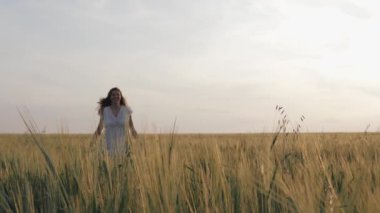 Gün batımında kırsal alanda koşan beyaz elbiseli mutlu kadın kollarını kaldırıyor.