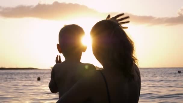 Silueta de mamá y bebé nadando en agua de mar saludan adiós a la puesta del sol — Vídeos de Stock