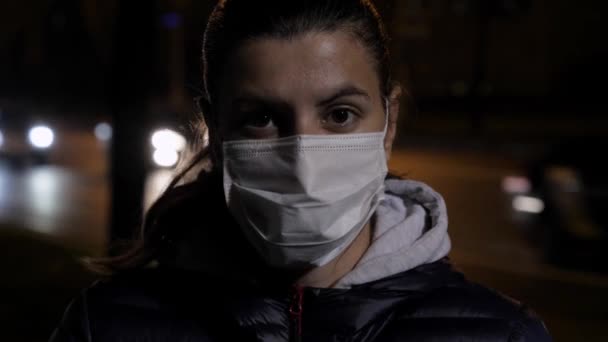 Портрет белой женщины в медицинской маске на лице, стоящей ночью у дороги — стоковое видео
