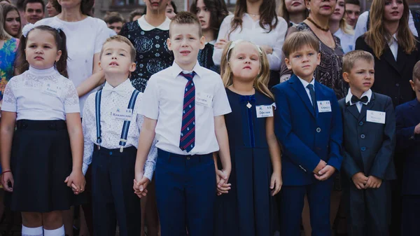 Zaporozhye, Ucrania - 1 de septiembre de 2018: los estudiantes de primer grado se paran en una regla al aire libre con maestros y estudiantes de secundaria en la línea de la escuela ceremonial el día del conocimiento . — Foto de Stock