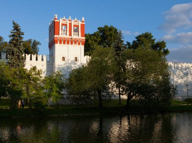 Kale duvarları ve kuleler, Moskova Novodevichy Manastırı suda yaz akşam gün batımına yansıtılır