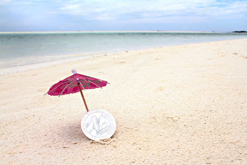 Silver Litecoin under the paper umbrella on the beach, shallow focus