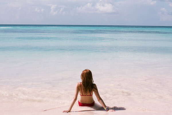Beautiful young woman sitting by the ocean, tropical beach