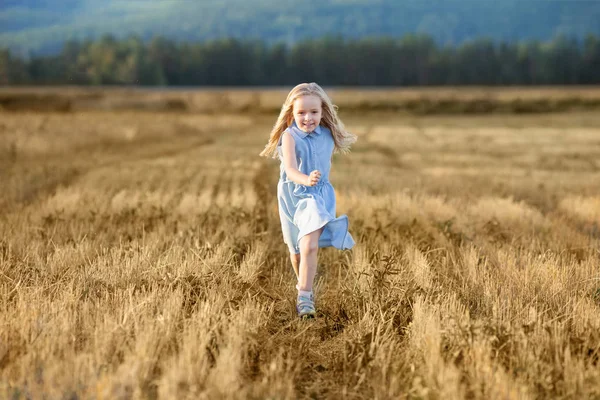 Küçük bir sarışın kız yaz aylarında bir buğday tarlasında koşuyor. — Stok fotoğraf