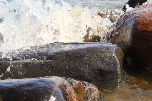 Розпилювач хвилі, що ламається на вологих каменях на березі — стокове фото