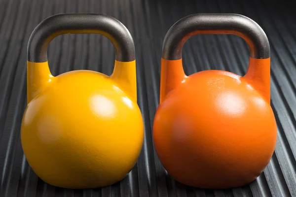 Kettlebells de levantamiento de peso amarillo y naranja dentro de un gimnasio — Foto de Stock