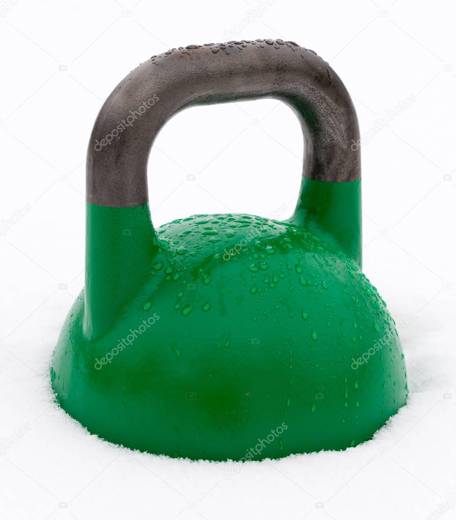 Green weight training kettlebell covered with water droplets outside in the snow