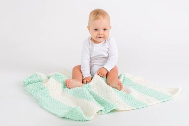 Beyaz arka planda, yumuşak çizgili, çift renkli battaniyeli gülümseyen çocuk.