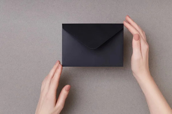 Composition of black envelope in female hands on the grey background