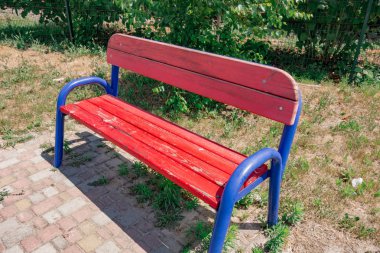 Parkta kırmızı ve mavi yıpranmış bank. Kamu oturma yeri ile 