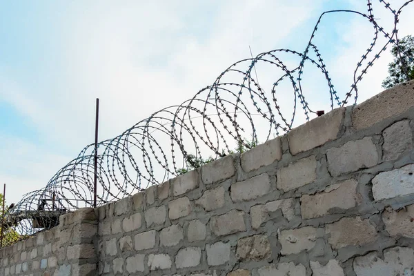 Barbed wire on brick wall or fence in front of blue sky. Concept
