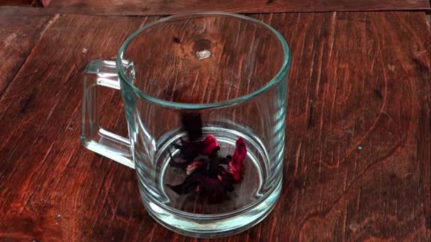 Hibiscus herbaty lub Sudan wzrosła ziołowe warzenie Roselle. Suszone kalyces jak liście i kwiaty są warzone w szklany przezroczysty kubek przebywających na Vintage drewniany stół — Wideo stockowe