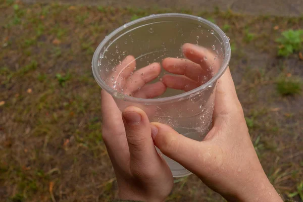 Glass with water droplets in kid hands. Boy collects rain drops — Stock Photo, Image