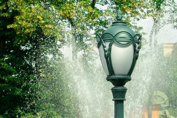 Ліхтар або паркове світло проти водяного струменя розбризкування з фонтану і — стокове фото