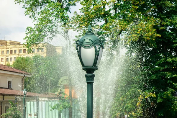 Ліхтар або паркове світло проти водяного струменя розбризкування з фонтану і — стокове фото