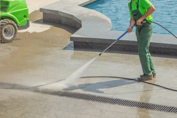 Worker man in uniform washes street or park sidewalk near water — Stock Photo, Image