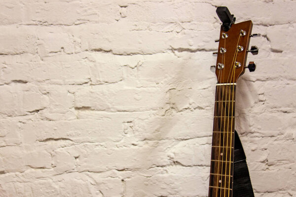 Guitar headstock and neck against white background. Musical instruments stands leaning on brick wall with empty copy space to add text of image. Music backdrop