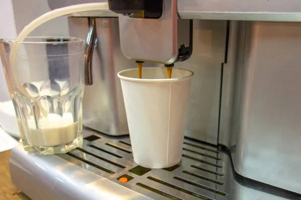 Coffee machine pouring hot drink into paper glass. White blank g