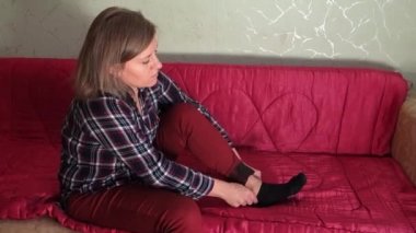 Kadın çorabını çıkarıp ayağına masaj yapıyor. Orta yaşlı ya da yaşlı beyaz bir kadın kanepede oturur. Yorgun ve ayakları ağrıyor. Kız mutsuz.