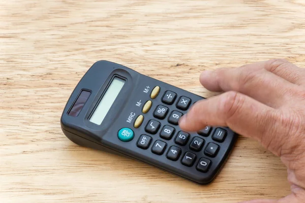Persona haciendo cuenta, en una calculadora de bolsillo con un fondo de madera . — Foto de Stock
