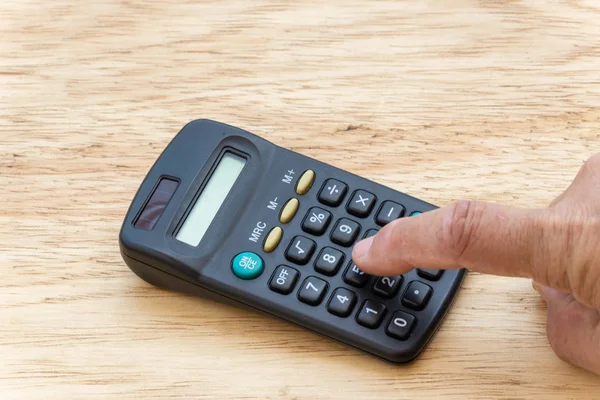 Persona haciendo cuenta, en una calculadora de bolsillo con un fondo de madera . — Foto de Stock