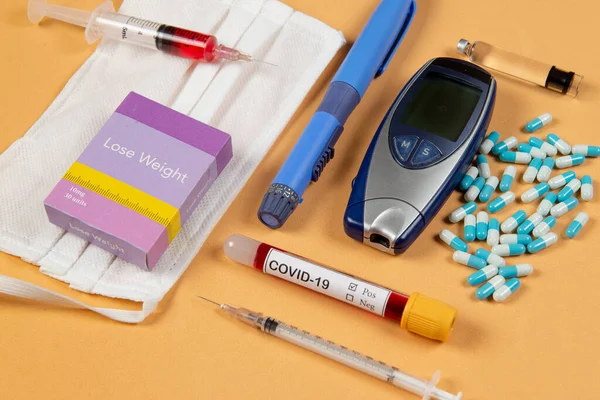 various elements of medicine on a orange background and a tube of blood test for covid-19
