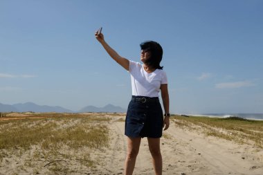 Yeni normal, orta yaşlı kadın plajın bir fotoğrafını çekiyor. Toplama olmadan, koruyucu bir maske takarak. Covid-19 'a