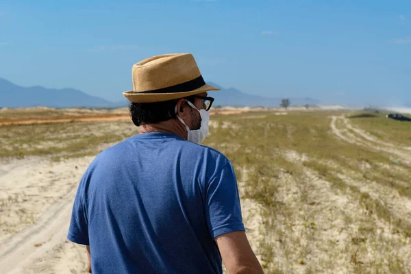 The new normal - man with hat walking through an area near the beach, looking at the horizon