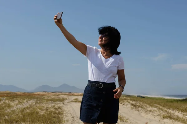 The new normal - middle-aged woman takes a selfie of the beach in a place without agglomeration, wearing a protective mask tells the covid-19