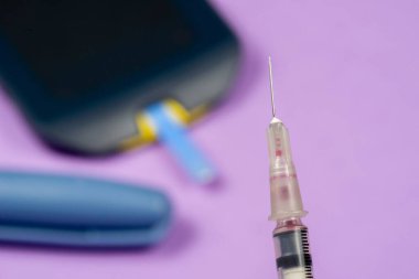 Ön planda insülin şırıngası, arka planda bulanık diyabet glukometresi
