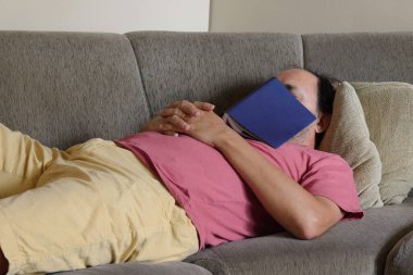 Orta yaşlı bir adam kanepede uyur ve üzerine kitap yazar.