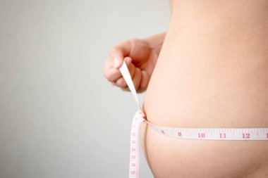 Adam göbeğini mezurayla ölçüyor.