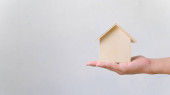 Ruka drží dřevěný dům. Investice do nemovitostí a hypotéky na bydlení finanční realitní koncept