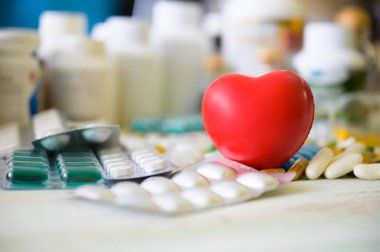 Ahşap masada kırmızı kalp ikonu, hap ve tablet ilacı. Sağlık sigortasını, sağlık sigortanızı,