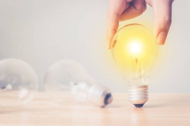 Ahşap masada el ele tutuşan ampul. Yenilik ve yaratıcılıkla yeni bir fikir oluştur