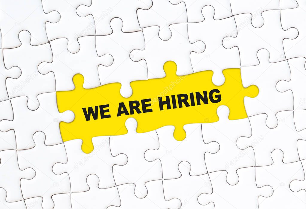 We are hiring concept. White jigsaw puzzle with word and yellow background