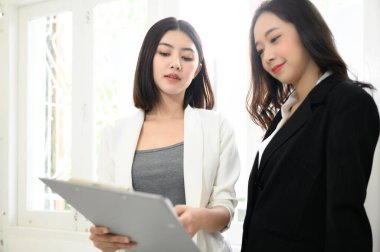 İki güzel Asyalı iş kadını iş yerinde iş hakkında konuşup eğleniyorlar.