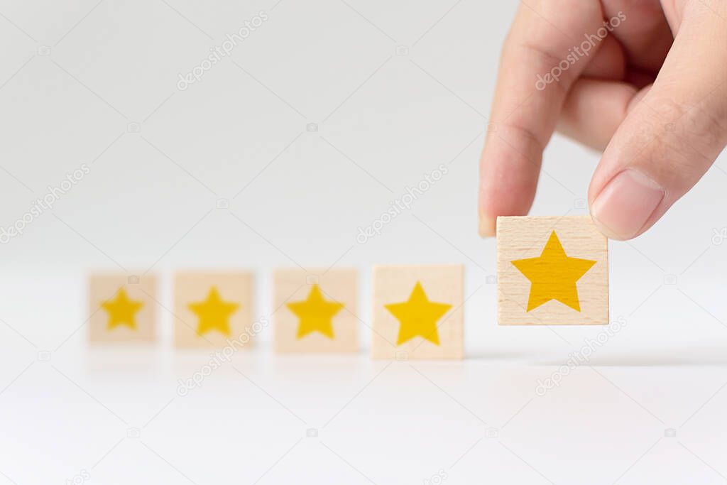 Hand putting wooden cube with five star shape on white background. The best excellent business services rating customer experience concept