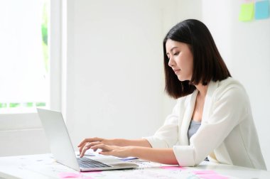Evden çalışma kavramı. Ofiste bilgisayarla çalışan Asyalı genç bir iş kadını ve masa başında evrak işleri var.