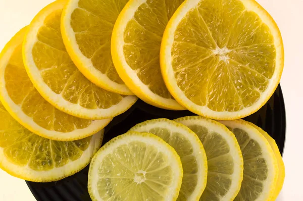 Rodajas de naranja y limón en un plato negro aislado sobre fondo blanco — Foto de Stock