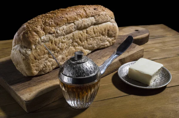 Bread and a knife on the kitchen board. And a glass of honey, a — Stock Photo, Image