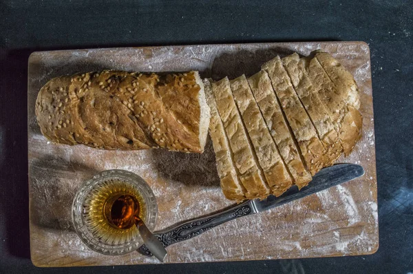 Fresh sliced wheat bran bread , glass of honey and knife on the — Stock Photo, Image