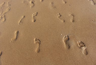 Güneşli bir günde ıslak deniz kumlarında ayak izleri ve güneş parlaması.