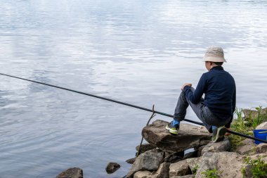 Çocuk bulutlu bir günde nehirde balık tutuyor.