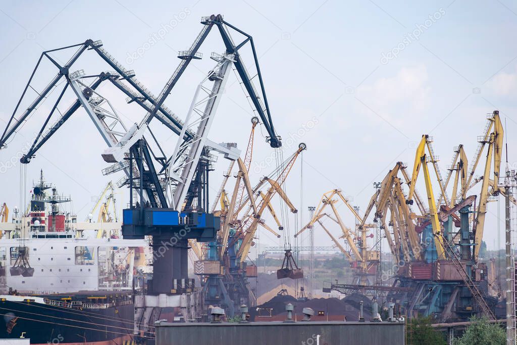 Cranes at the cargo sea port loading the bulk carrier with iron ore or coal