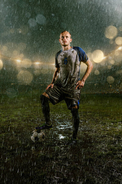 Soccer player on professional soccer night rain stadium. Dirty player in rain drops with football ball