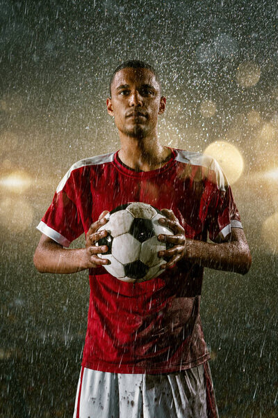 Soccer player on professional soccer night rain stadium. Dirty player in rain drops with football ball