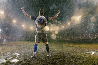 Profesyonel futbol gece yağmur stadyumda futbolcu. Yağmurdaki kirli oyuncu duygusal olarak zafere sevinir. Geri görünüm