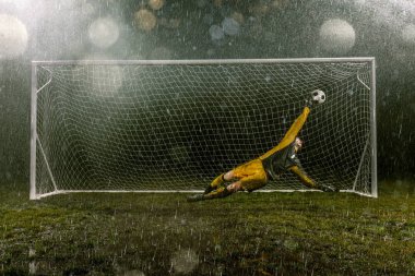 Dirty goalkeeper in flight catch the ball. Professional night rain stadium with football goal. Grass in the stadium wet from the rain clipart